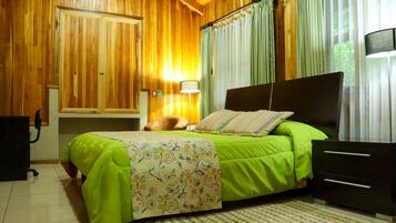 A bedroom with a wooden ceiling, a bed with a green bedspread, a nightstand, a lamp, and a window with curtains.