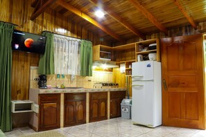 A kitchen with wooden cabinets, a microwave, a refrigerator, and a television mounted on the wall.
