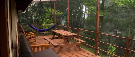 Un terrazzo in legno con un'amaca, un tavolo da picnic e una zona relax con vista su un paesaggio boschivo.