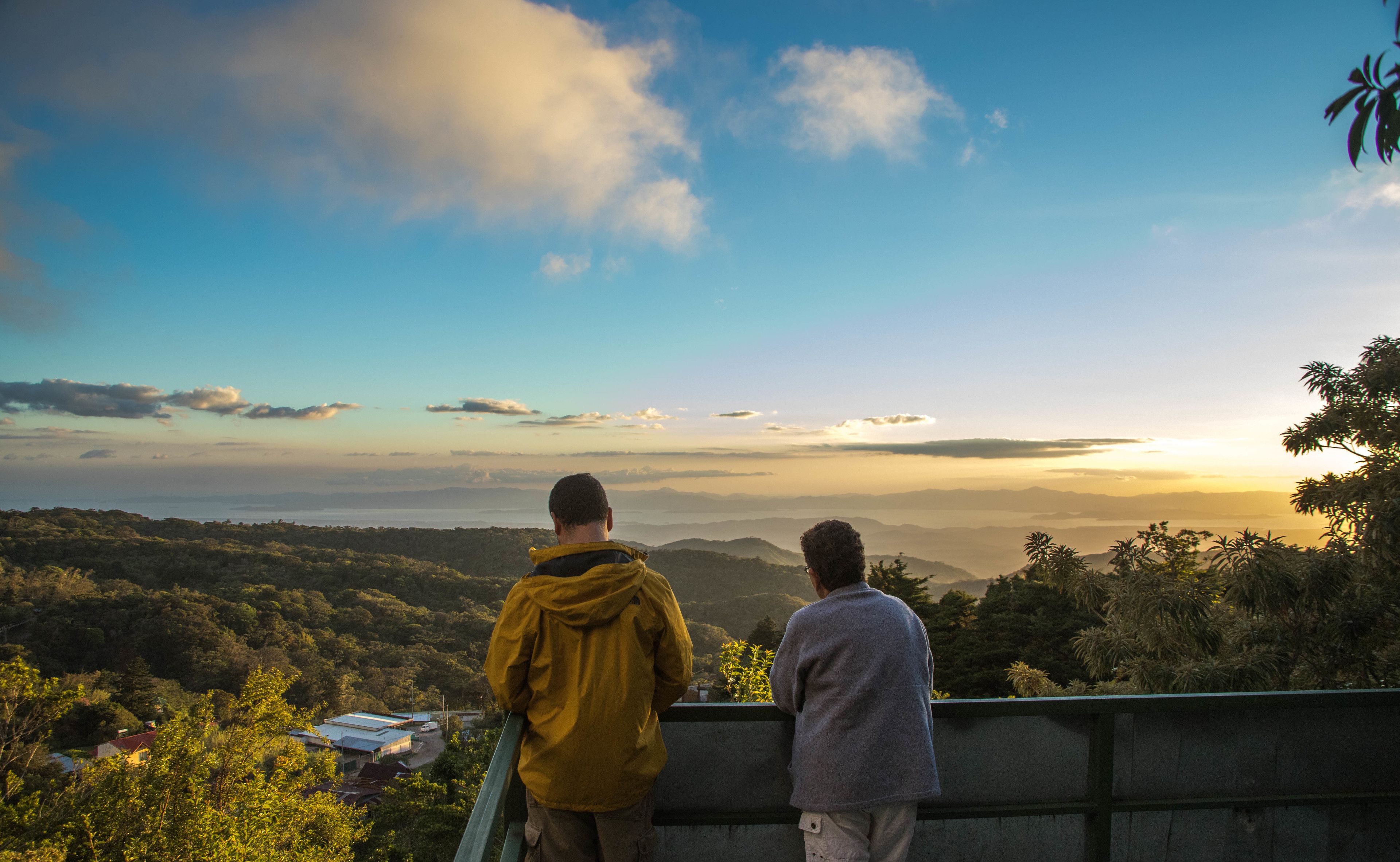 Two people overlooking a scenic landscape with mountains and a body of water in the distance.