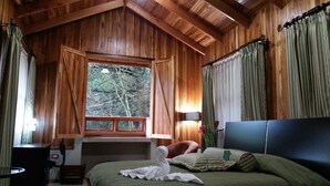 Een houten slaapkamer met een bed, een bureau en een raam met uitzicht op een bos.