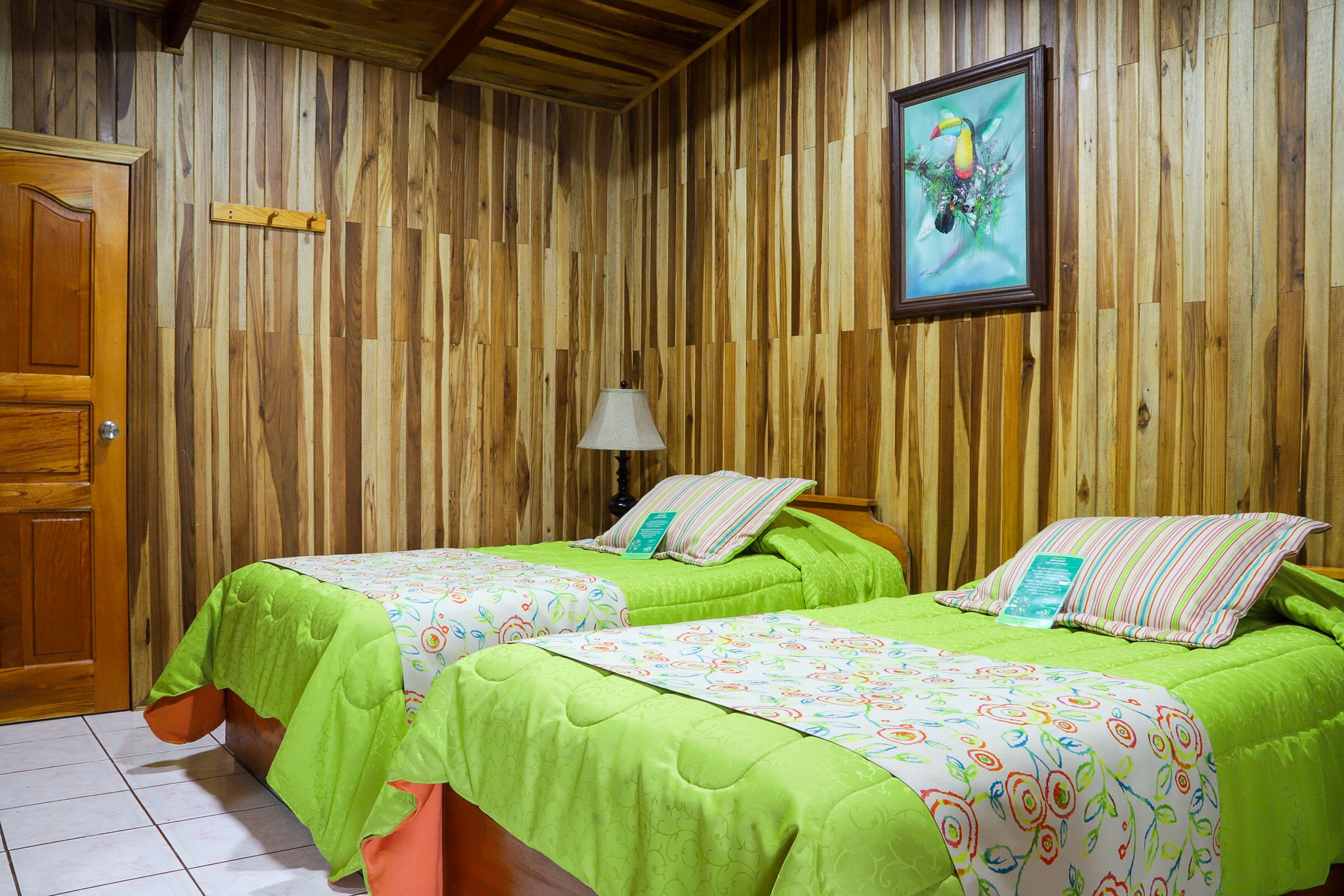 A room with two beds, wooden walls, a wooden door, and a painting on the wall.