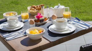 Mesa para desayunar al aire libre con croissants, fruta, café y jugo.