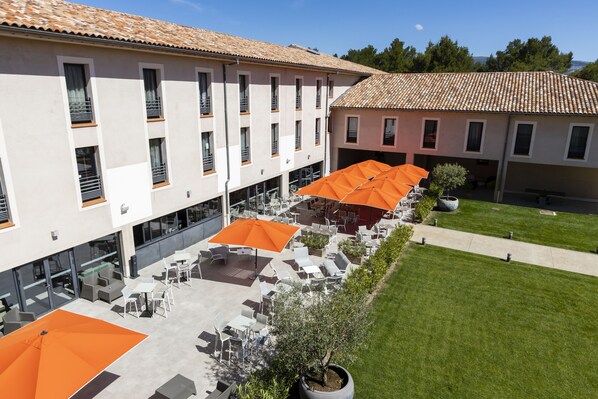 Un espacio al aire libre con mesas y sillas, sombrillas anaranjadas y un edificio con techo de tejas.