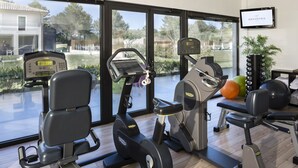 Un gimnasio con diversos equipos de ejercicio, un ventanal con vistas al exterior y una pantalla de televisión mostrando 'Grand Prix'.