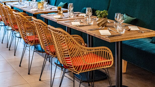 Un restaurante con largas mesas de madera, sillas de mimbre y un sofá color turquesa.