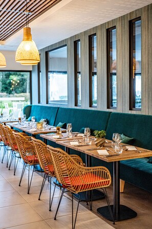 Un restaurante con largas mesas de madera, sillas de mimbre y un sofá color turquesa.