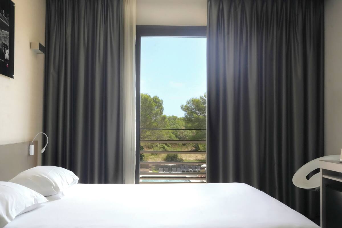 A hotel room with a bed, a desk, and a window with curtains.