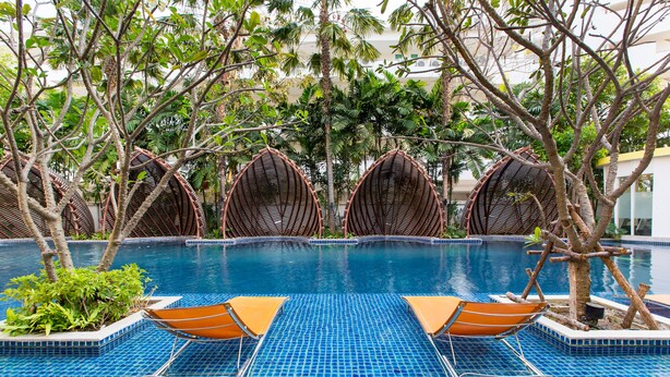 A pool area with blue-tiled flooring, wicker lounge chairs, and surrounding greenery. - Mykonos Beach Apartment (Hua Hin)