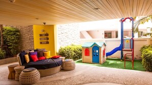 A cozy outdoor seating area with a sofa and ottomans, a children's play structure, and a stone wall. - Mykonos Beach Apartment (Hua Hin)