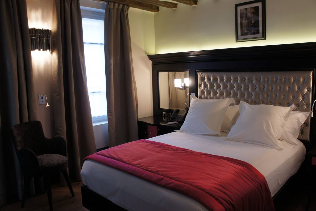 A hotel room with a large bed, a chair, a bedside table, and a lamp.