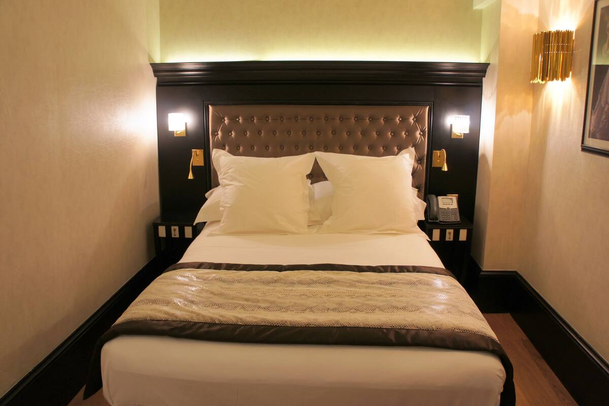 A hotel room with a large bed, a wooden headboard, bedside lamps, and a telephone on the nightstand.