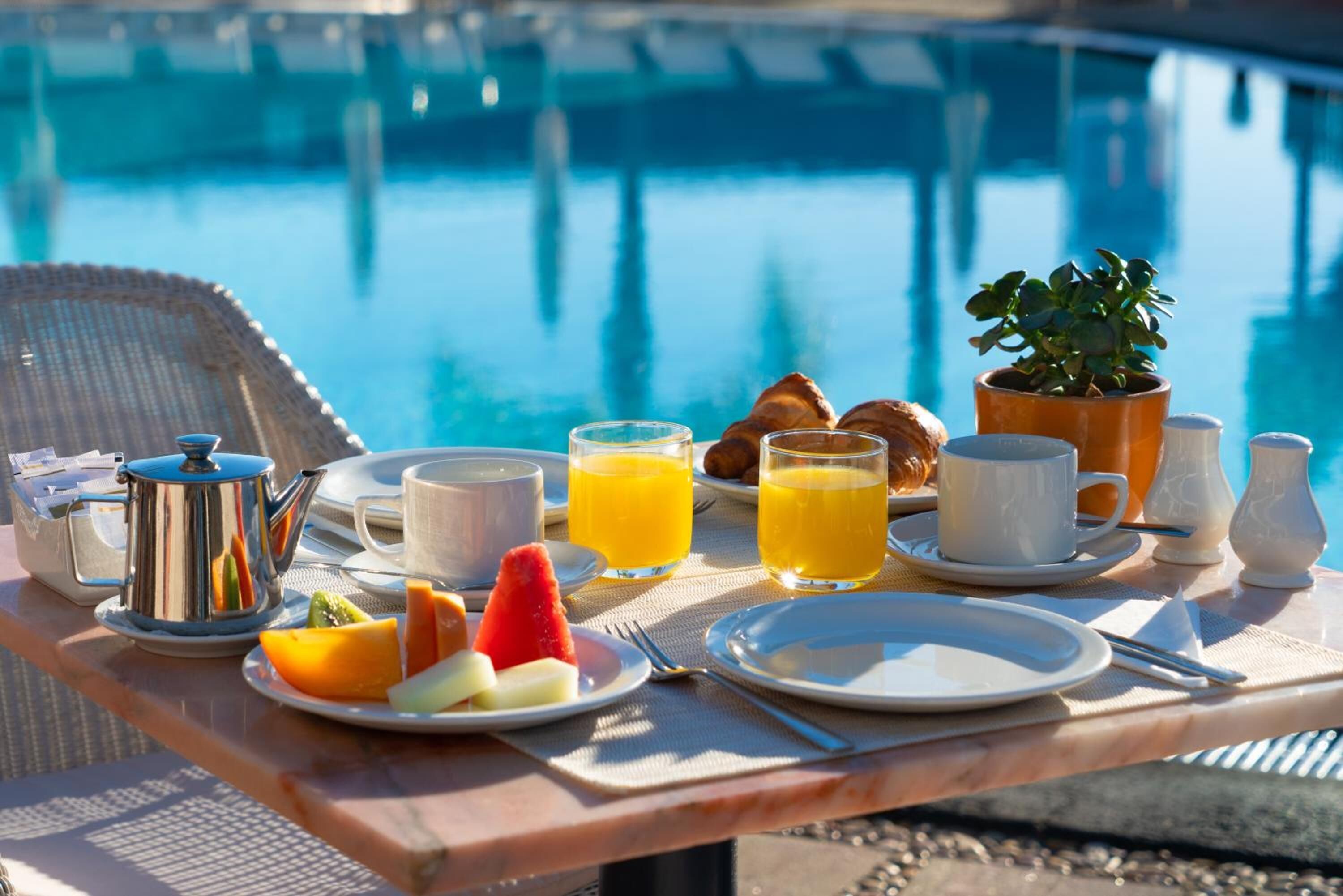 Een ontbijt bij het zwembad met croissants, fruit, sap en koffie.