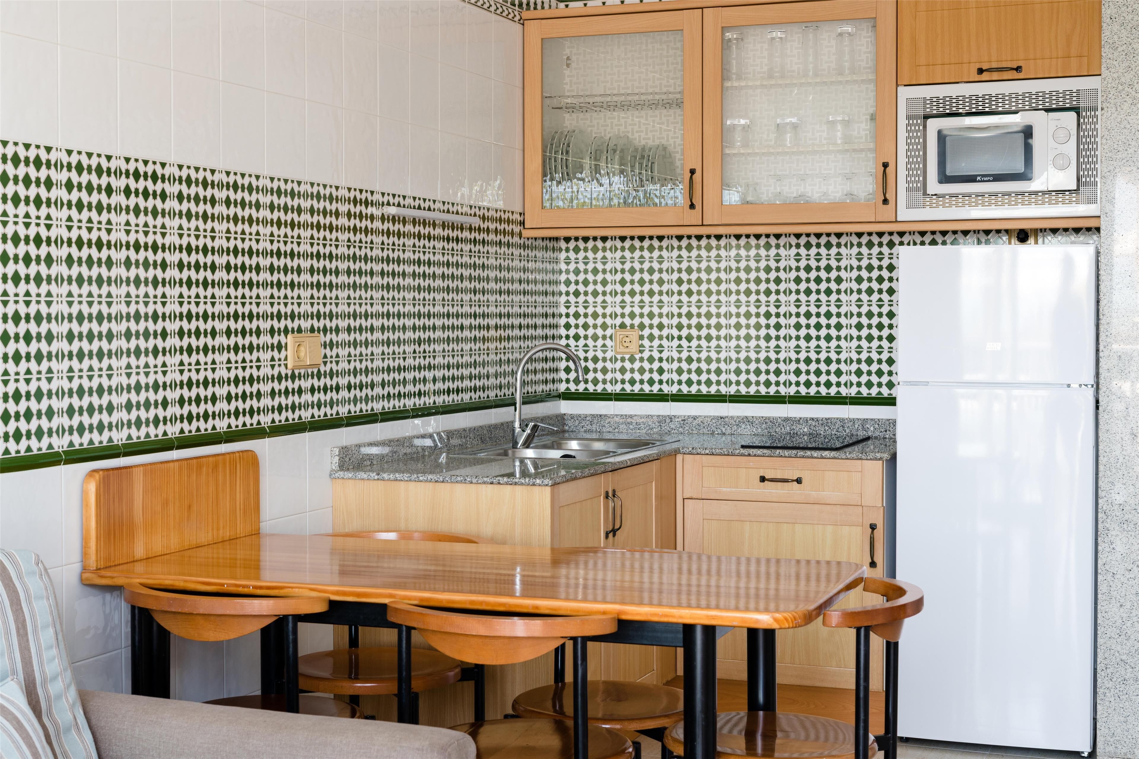 Una cocina compacta con una mesa y sillas de madera, un microondas y un refrigerador.