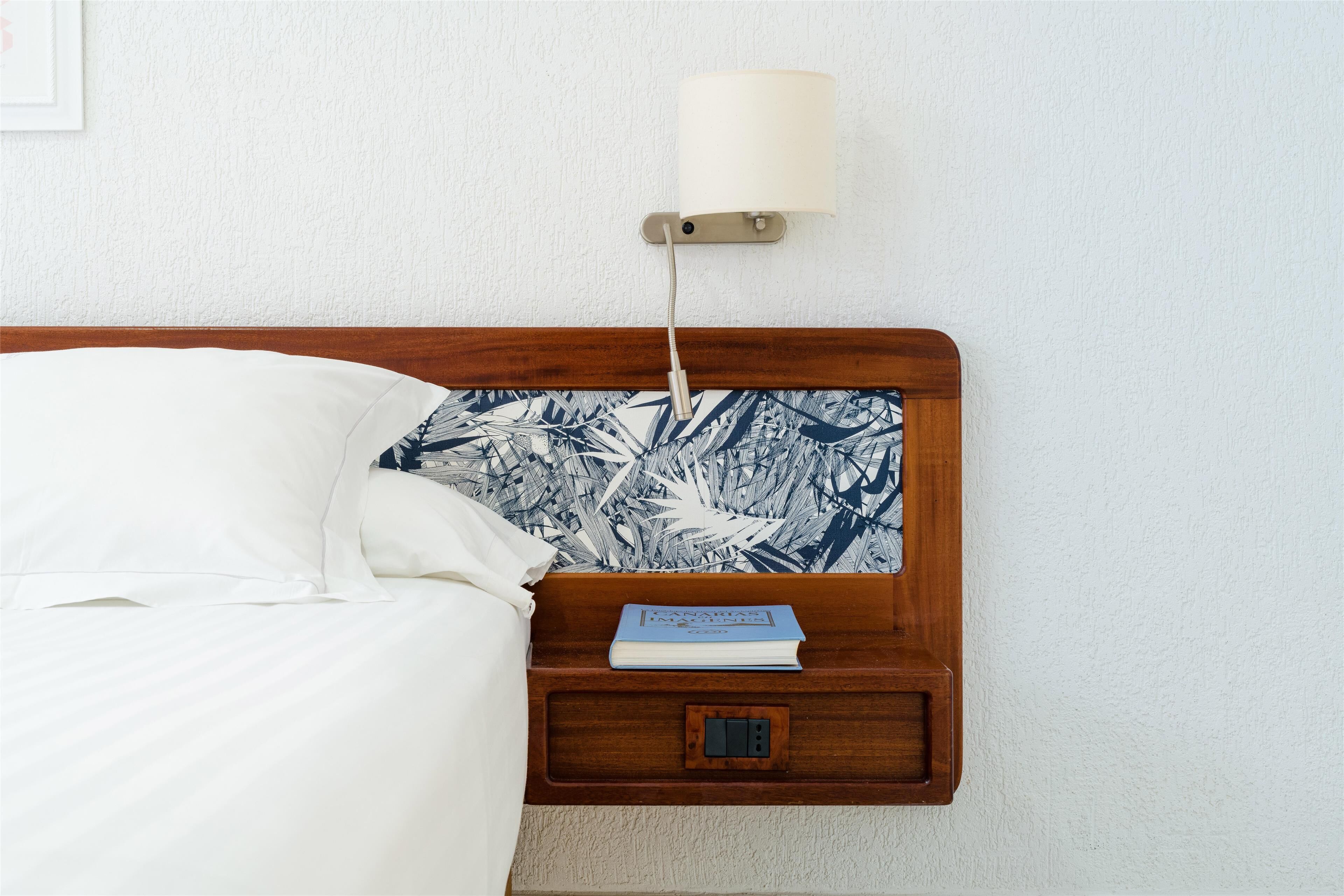 A neatly made bed with white linens, a wooden headboard, and a bedside table with a book and a lamp.