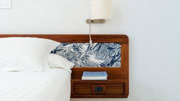 A neatly made bed with white linens, a wooden headboard, and a bedside table with a book and a lamp.