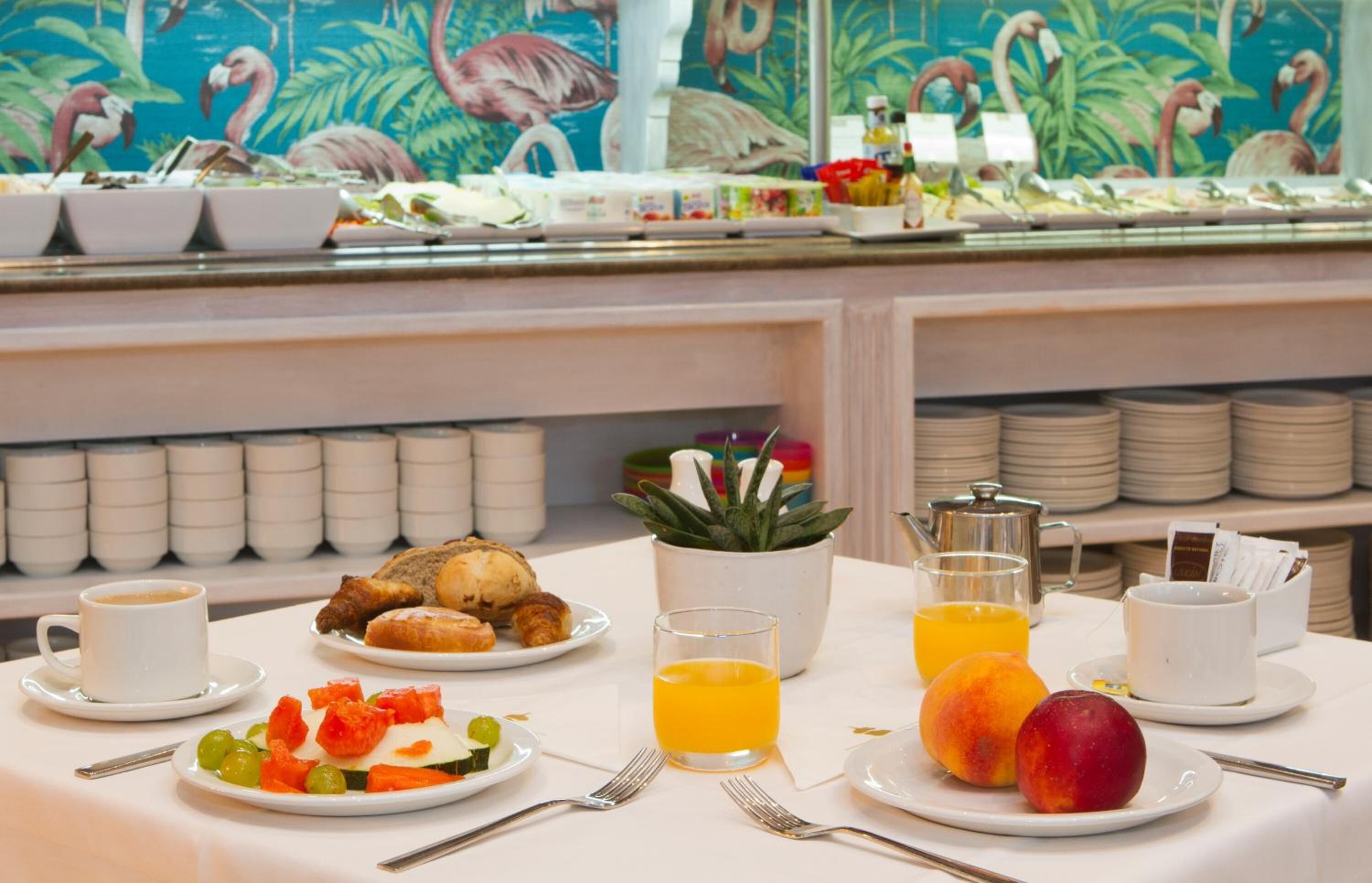 Un bufé de desayuno con diversos platos, entre ellos frutas, pasteles y una estación de café.