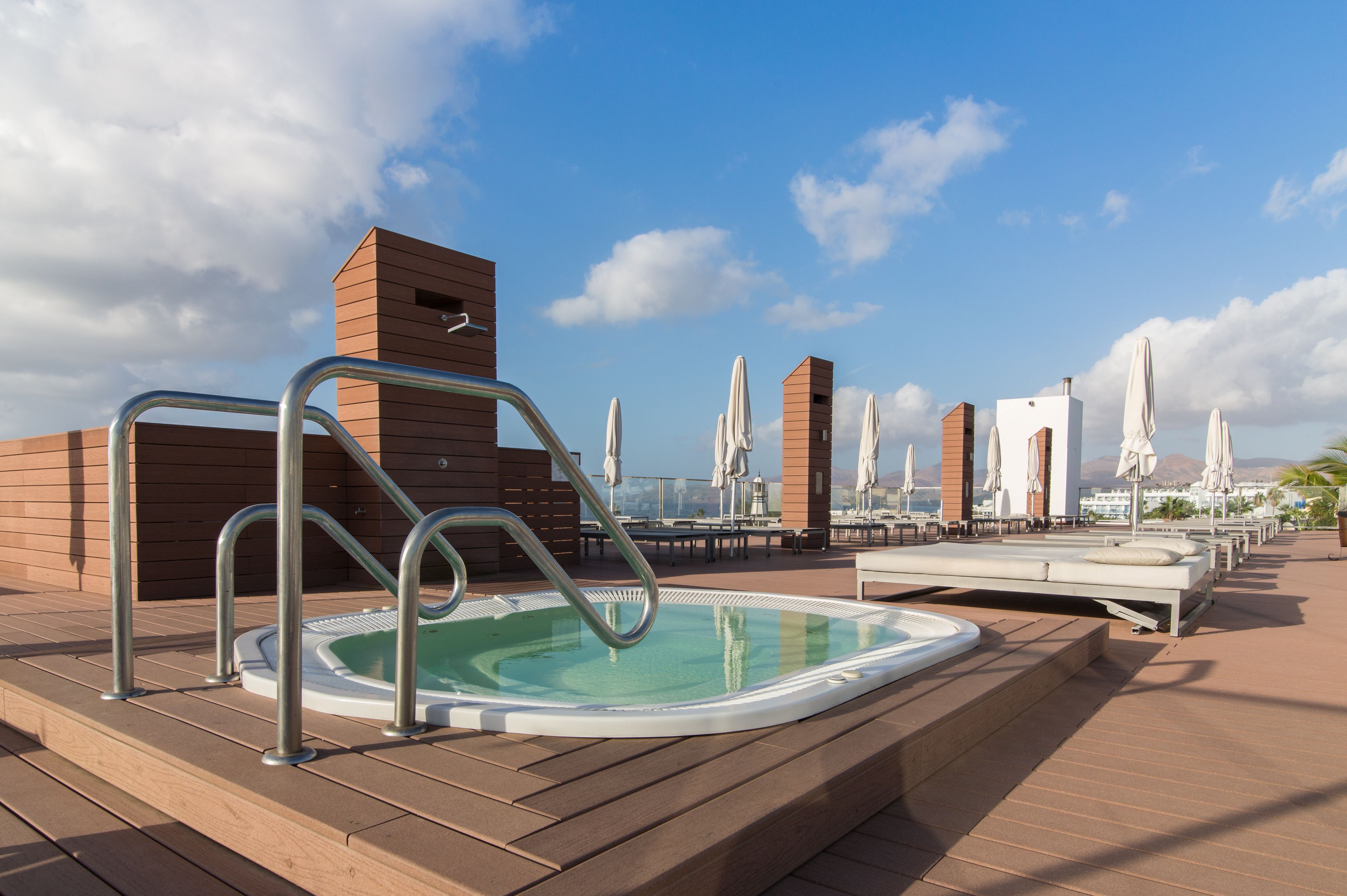 Un área de piscina en la azotea con un jacuzzi, sillas de descanso y sombrillas.