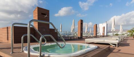 Un área de piscina en la azotea con un jacuzzi, sillas de descanso y sombrillas.