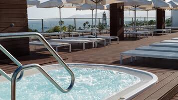 A rooftop pool area with a hot tub, lounge chairs, and umbrellas.