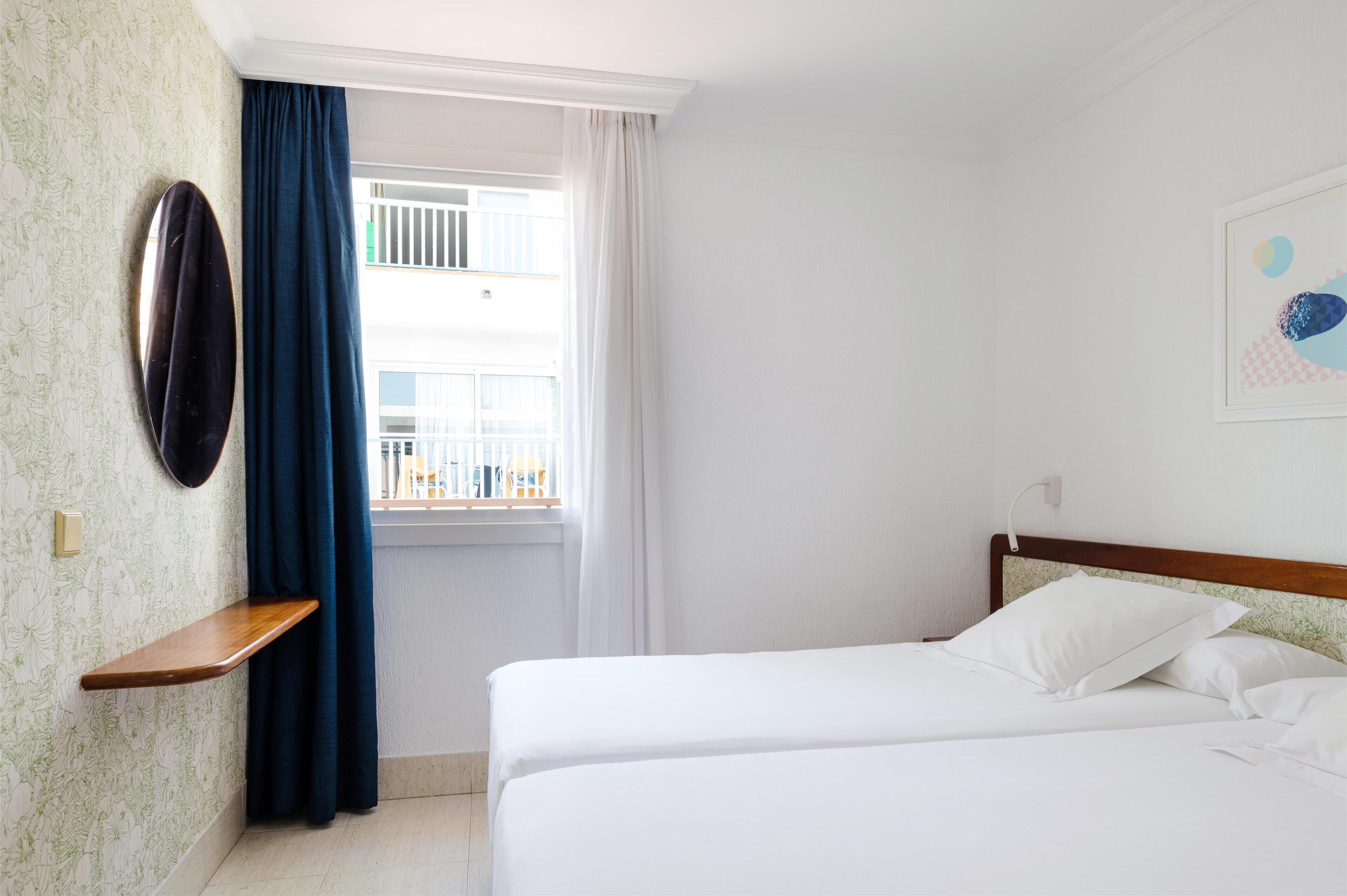 A hotel room with two beds, a window with curtains, a wall-mounted shelf, and a framed picture.