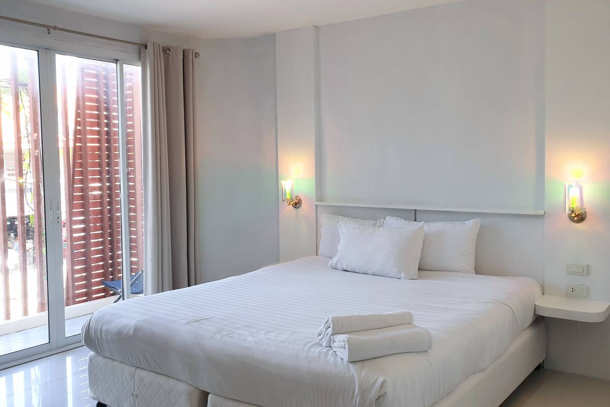 A neatly made bed with white linens, a headboard, and two wall-mounted light fixtures.