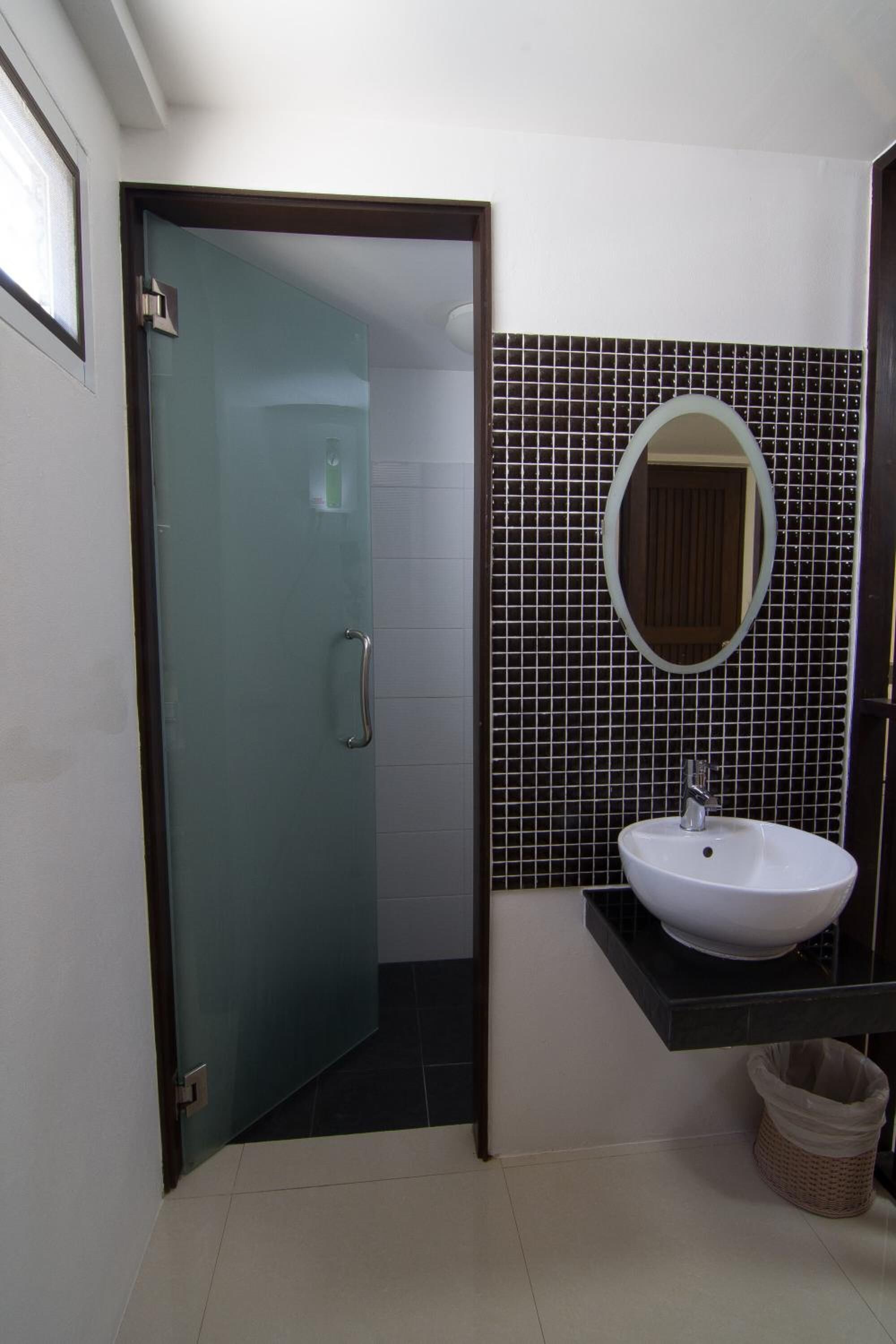 A bathroom with a glass door, a white sink, a mirror, and a tiled wall.