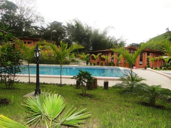 A pool area with a brick building, surrounded by greenery and a lamp post. - Hostería Sumak Pakari (Nanegalito)