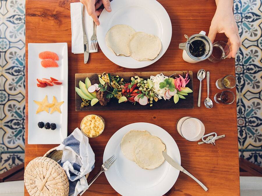 A dining table with plates of food, a bottle of sauce, and a woven basket.