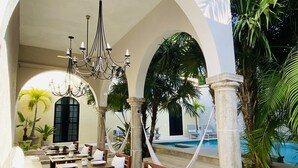 Un espacio de comedor al aire libre con mesas y sillas, una araña y una piscina al fondo.