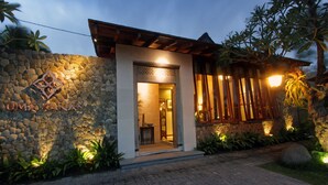 A modern building with a stone facade, a wooden entrance, and a well-lit interior. - Uma Karan (Seminyak)