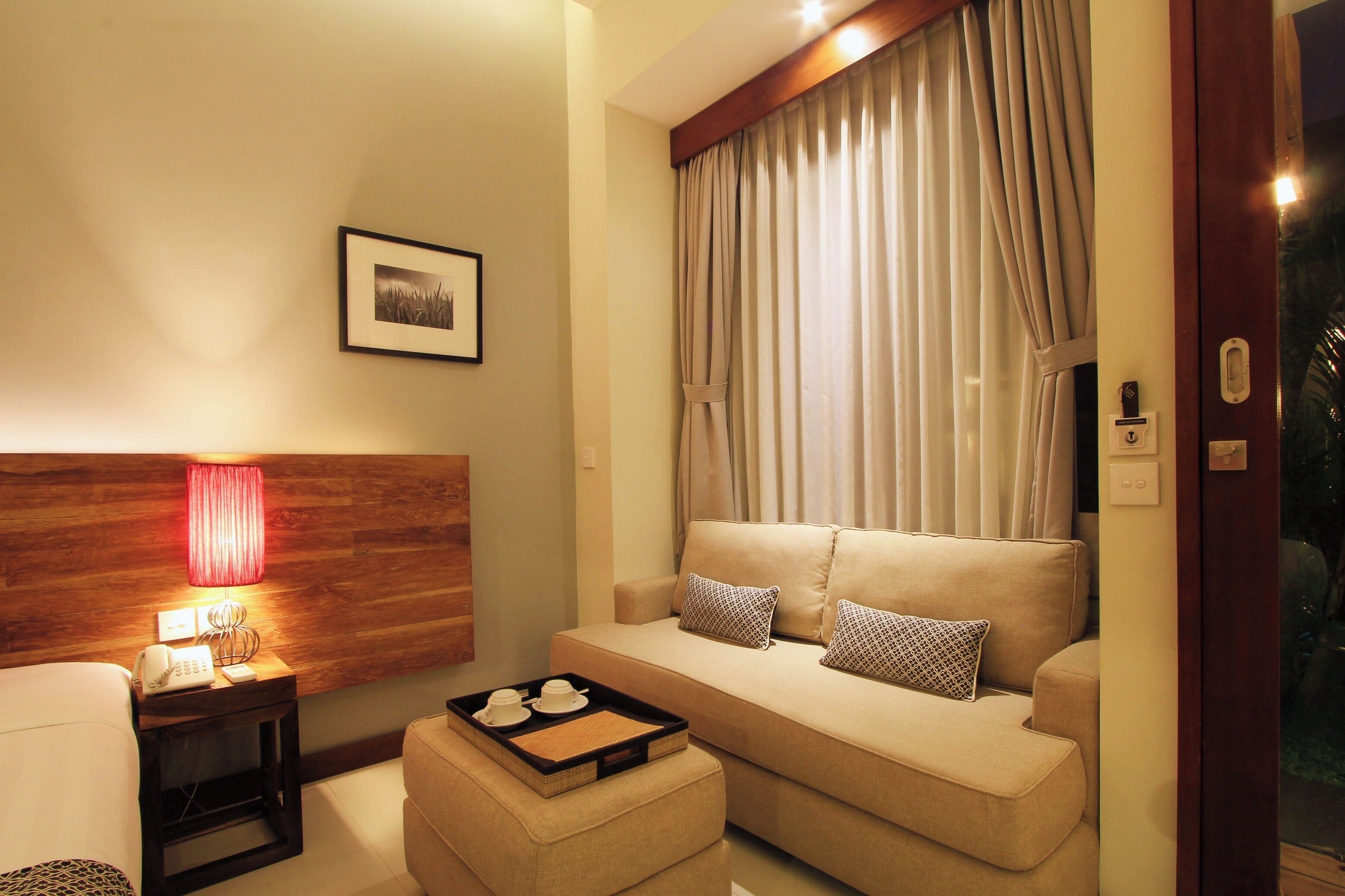 Quarto de hotel com sofá, mesa de cabeceira com luminária, bandeja com xícaras e um quadro pendurado na parede.