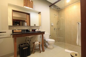 Casa de banho moderna com chuveiro separado por vidro, sanita e zona de lavatório com espelho e porta-toalhas.