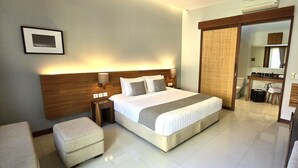 A hotel room with a bed, bedside tables, a chair, a desk, a mirror, and a sliding door leading to a bathroom. - Uma Karan (Seminyak)