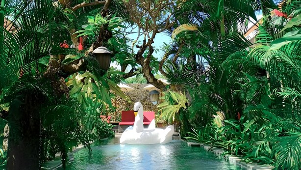 A serene indoor pool area surrounded by lush tropical foliage, with a swan-shaped float in the water. - Uma Karan (Seminyak)