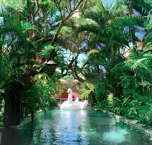 Un área de piscina interior tranquila rodeada de exuberante follaje tropical, con un flotador con forma de cisne en el agua.