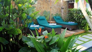 A garden with two lounge chairs, a stone wall, and lush greenery. - Uma Karan (Seminyak)