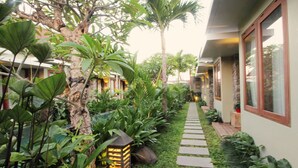 A pathway lined with tropical plants leading to a building with large windows and a stone wall. - Uma Karan (Seminyak)
