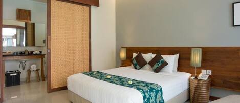 A hotel room with a large bed, a wooden headboard, a bedside table, a mirror, and a small round table.