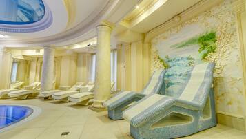 A luxurious spa area with reclining chairs, a pool, and ornate wall decorations.