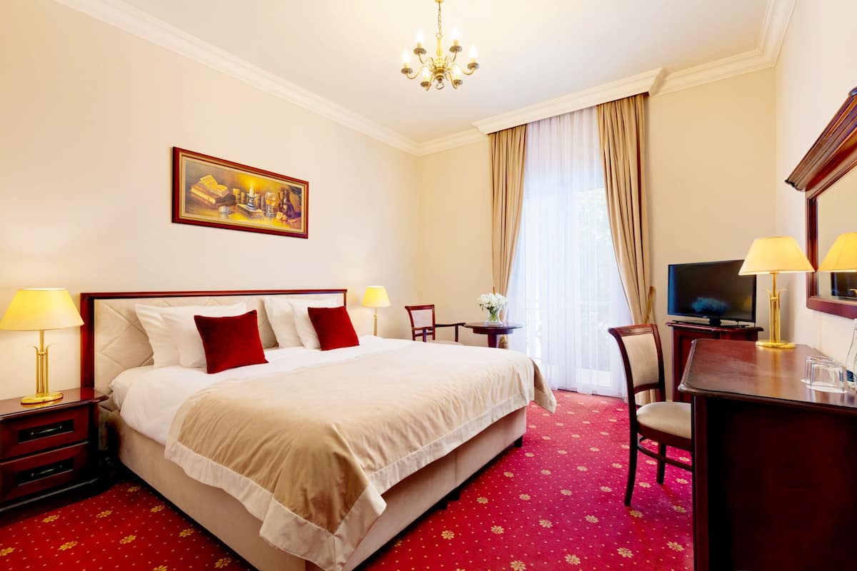 Habitación de hotel con una cama grande, un escritorio con televisor, una araña y un cuadro en la pared.