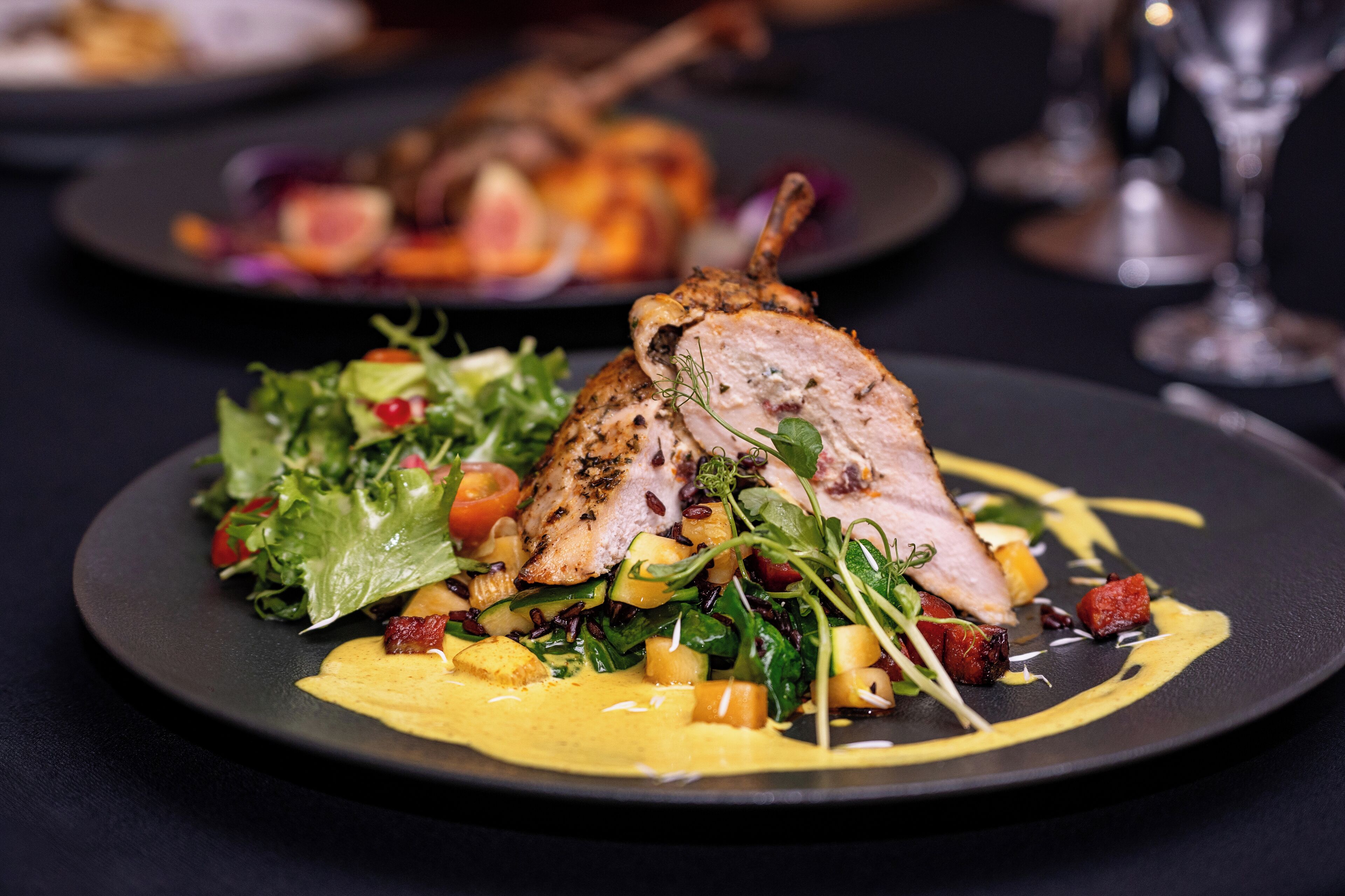 A plate of food with a roasted duck, greens, and a yellow sauce.
