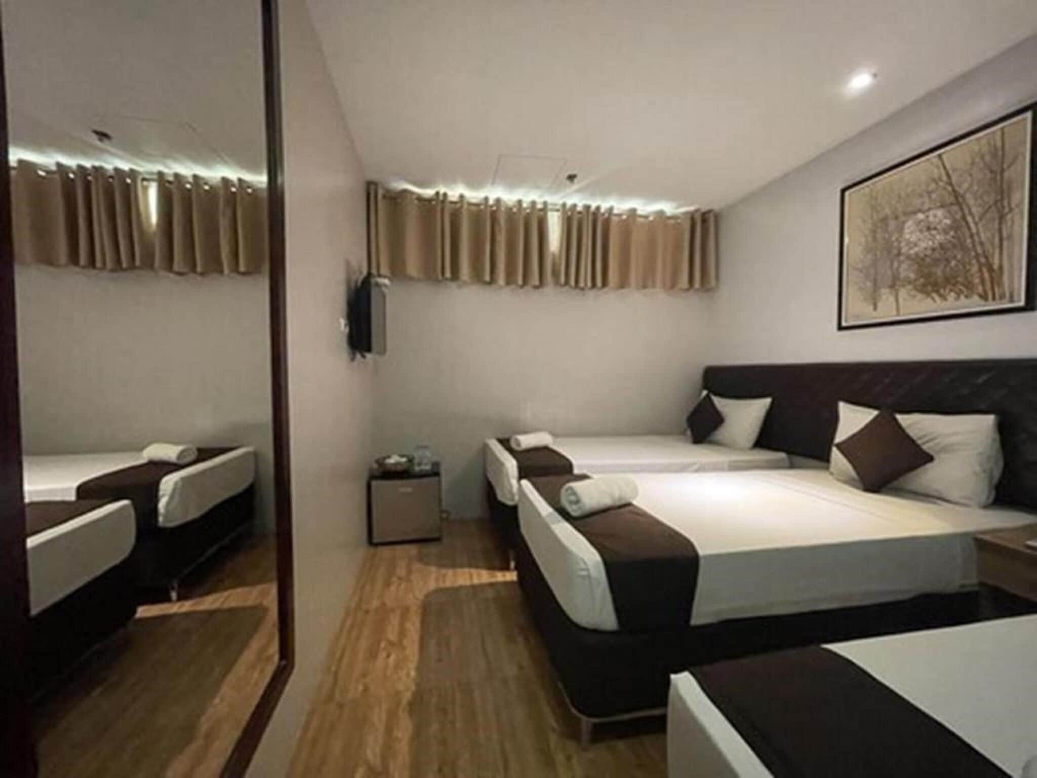 Une chambre d’hôtel avec deux lits, une petite table de chevet, un téléviseur fixé au mur et un tableau encadré.