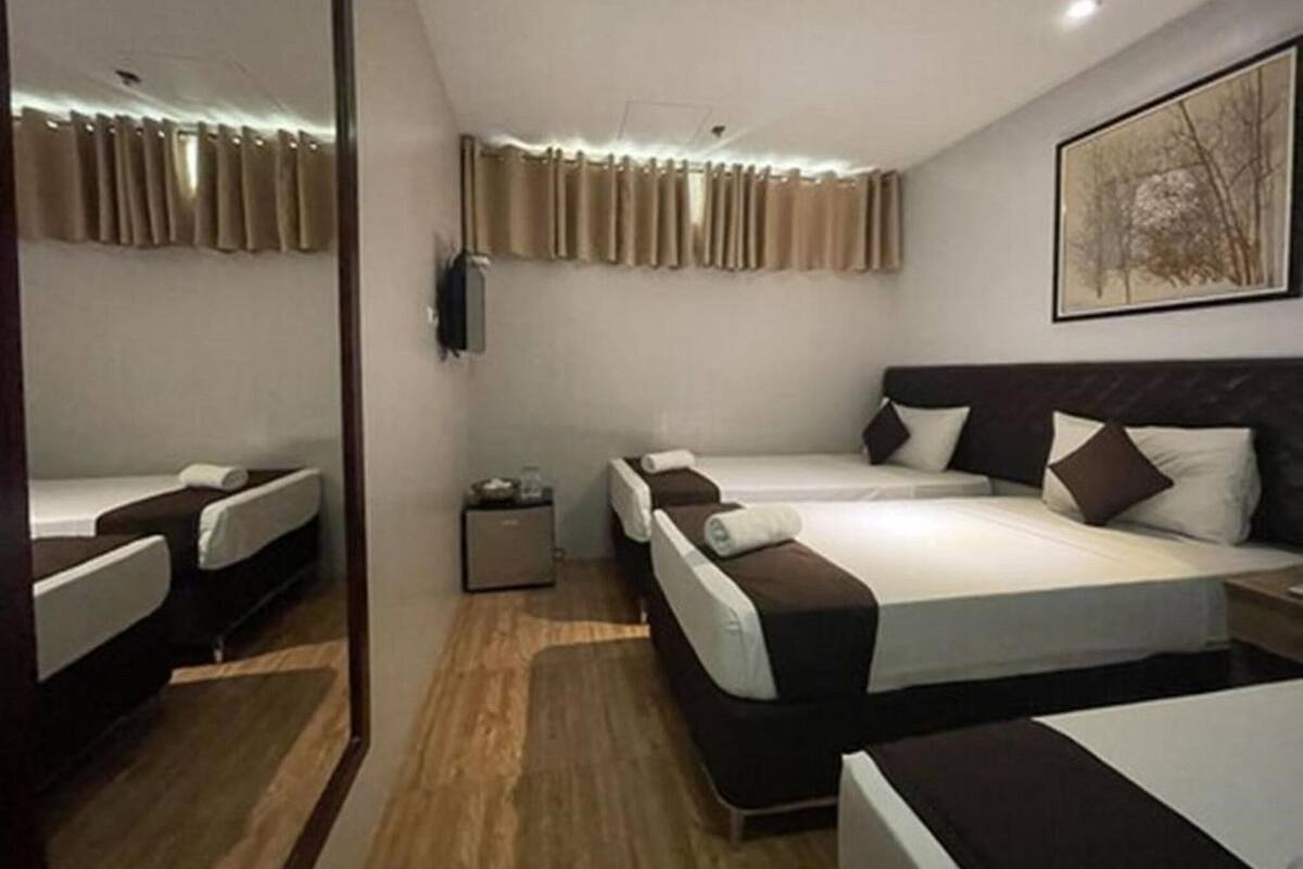 Quarto de hotel com duas camas, uma mesinha de cabeceira, televisão na parede e um quadro emoldurado.
