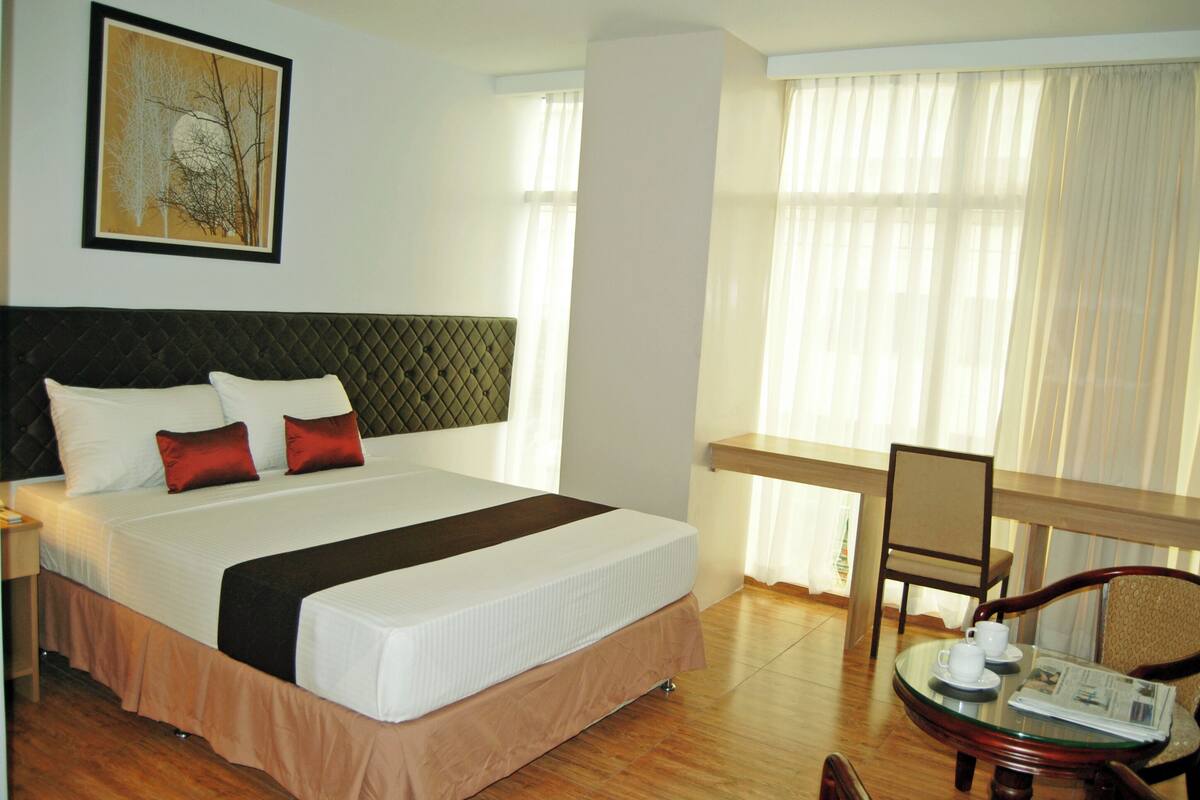 A hotel room with a bed, a desk, a chair, and a window with curtains.