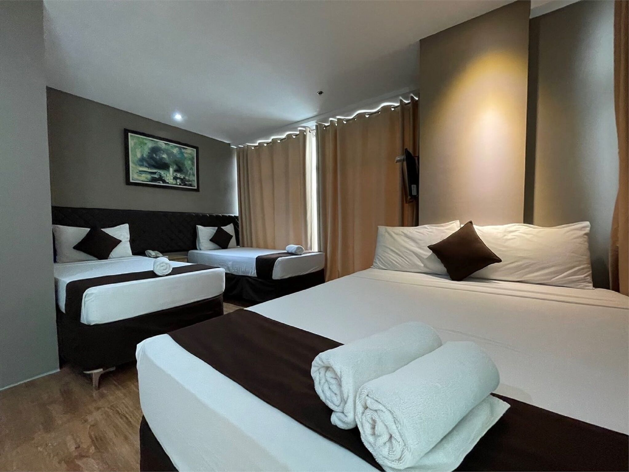 Une chambre d’hôtel avec deux lits, un bureau, une chaise, un tableau au mur et une fenêtre avec des rideaux.