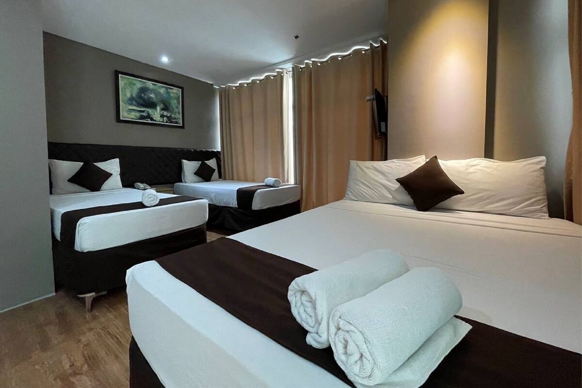 A hotel room with two beds, a desk, a chair, a painting on the wall, and a window with curtains.