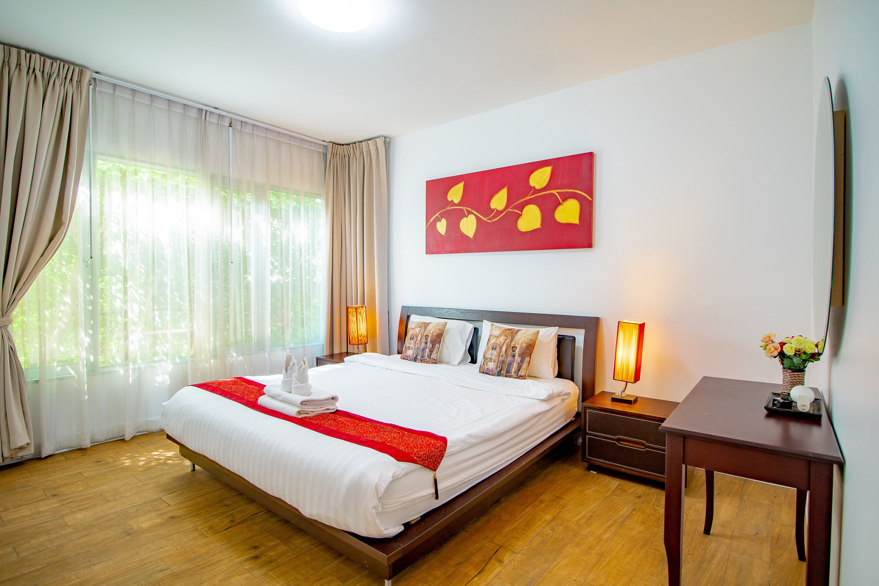 Une chambre d’hôtel avec un grand lit, une table de chevet avec une lampe, une petite table ornée de fleurs et un tableau accroché au mur.