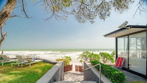Vista de la playa con una escalera que lleva a un edificio de fachada de vidrio, con vistas al océano.