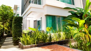 Un edificio moderno con balcón, ventanas amplias y un jardín con diversas plantas.